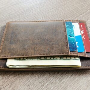 A brown leather wallet with cash and credit cards on a wooden surface.